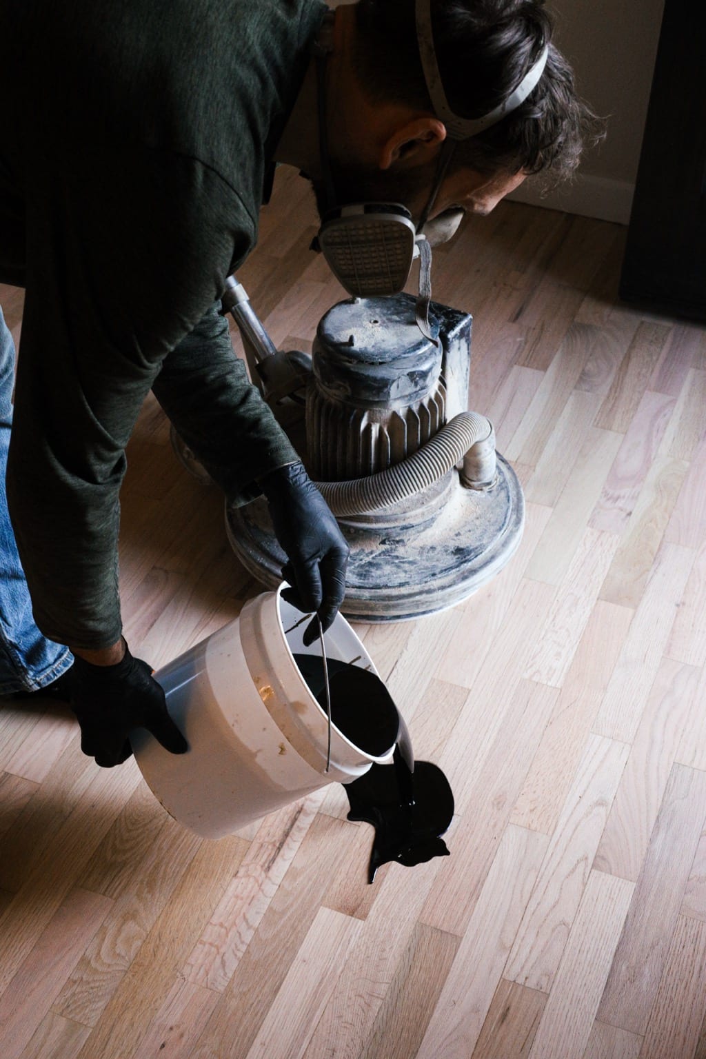 Craftsman in respirator pouring stain during hardwood floor refinish, Coeur d’Alene Idaho